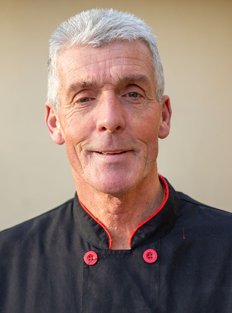 Peter Teale in a black chef's jacket with red buttons, smiling.