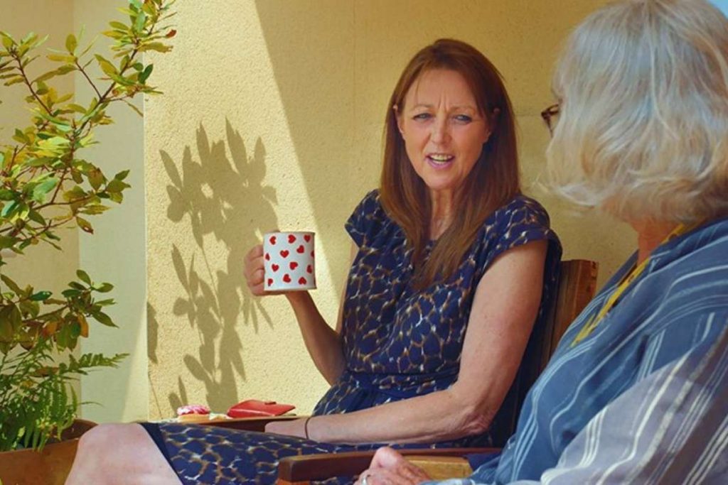 Two women chatting over coffee on the Skanda Vale Hospice patio.