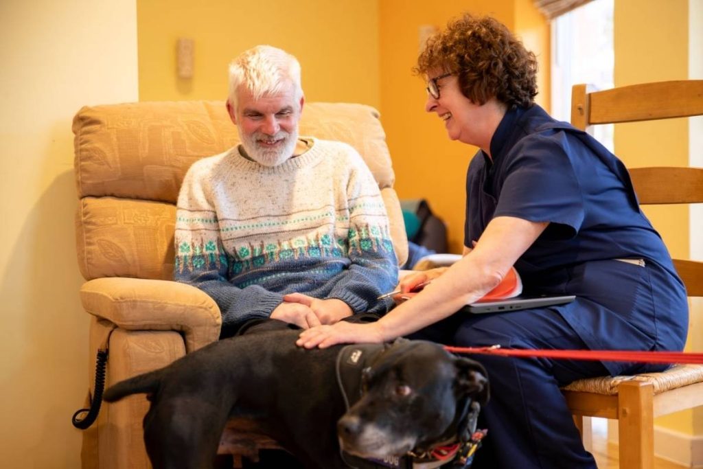 A nurse pets a dog next to a man at Skanda Vale Hospice.