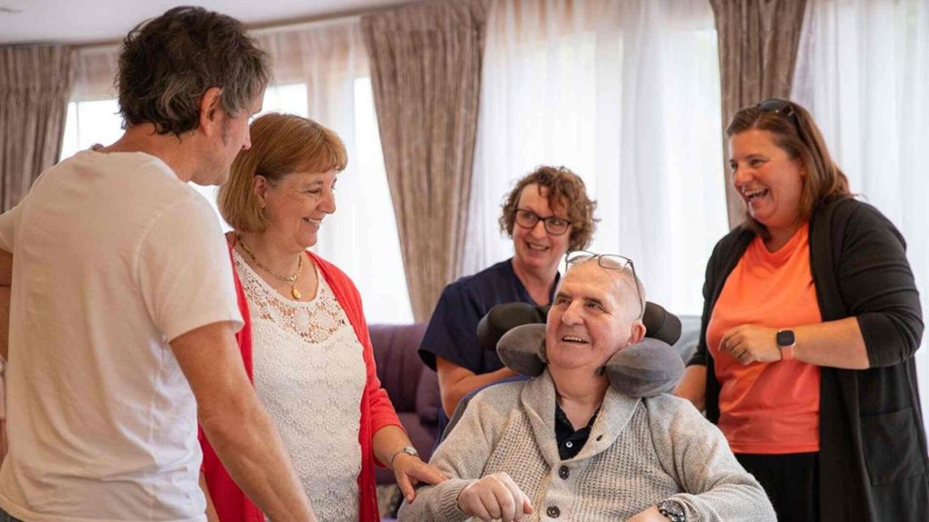 Volunteers, family members and patient of Skanda Vale Hospice sat together smiling.