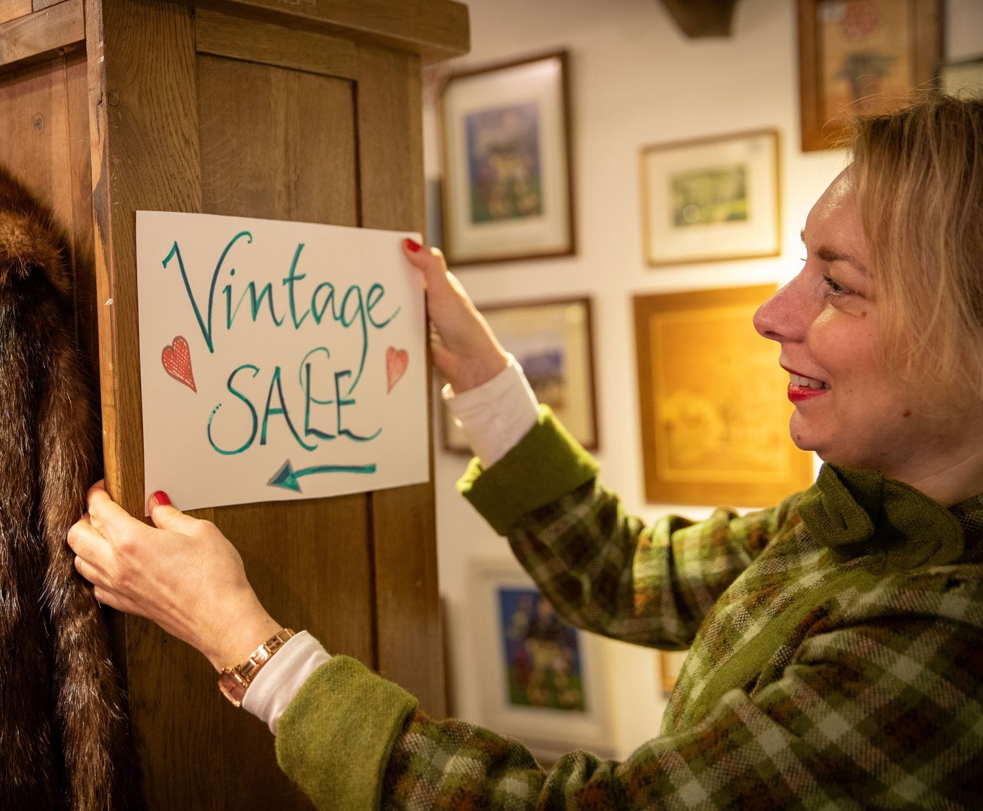 Hospice shop volunteer with a handwritten 'vintage sale' sign
